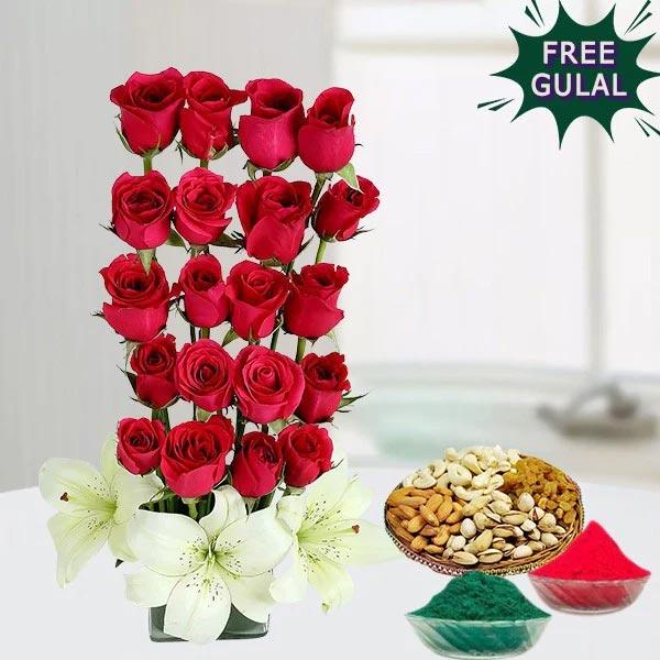 Tall arrangement of red roses with a bowl of dry fruits and colored powders on a white surface.