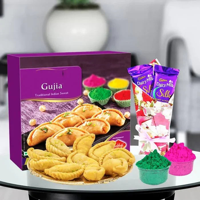 Box of Gujia with Cadbury Dairy Milk Silks and colorful powders on a table.