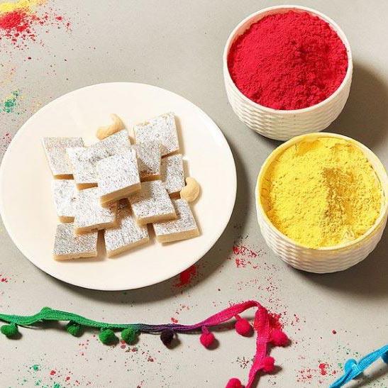 Square cookies on a plate with bowls of red and yellow powders on a light gray background.