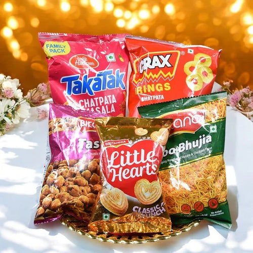 Assorted snack packages including Takatak, Crax, and Anso on a decorative surface with flowers.