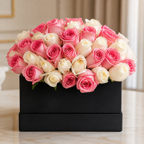Bouquet of pink and white roses in a black box on a marble surface.