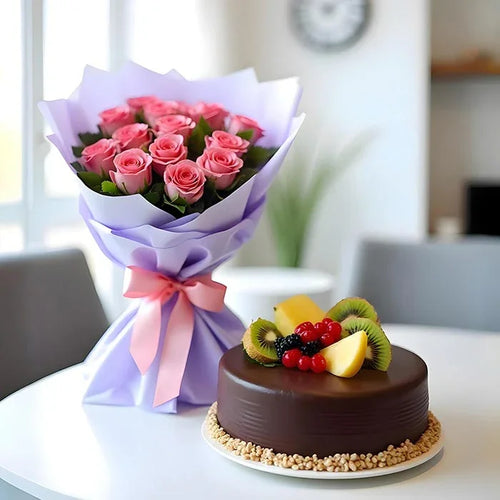 Chocolate cake with fruit decoration and a bouquet of pink roses on a table.