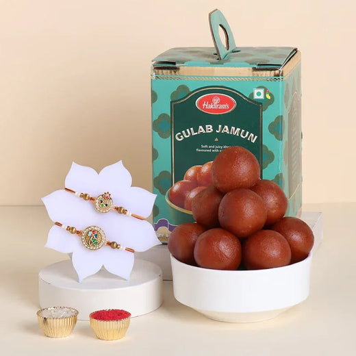 Bowl of Gulab Jamun with Halka Halka packaging, white flowers, and gold items on a beige background
