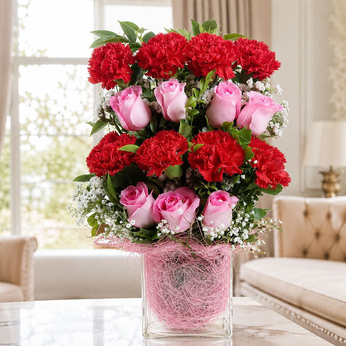 Bouquet of red carnations and pink roses in a clear vase on a table with a blurred background