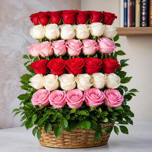 Stacked arrangement of red, white, and pink roses in a basket on a neutral background
