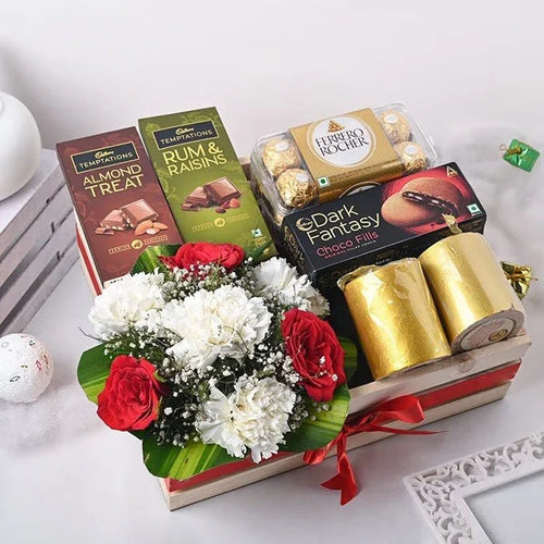 Gourmet gift basket with chocolates, flowers, and gold ribbons on a white surface.