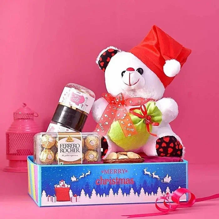 Christmas-themed gift set with teddy bear, Ferrero Rocher chocolates, and candy on a pink background