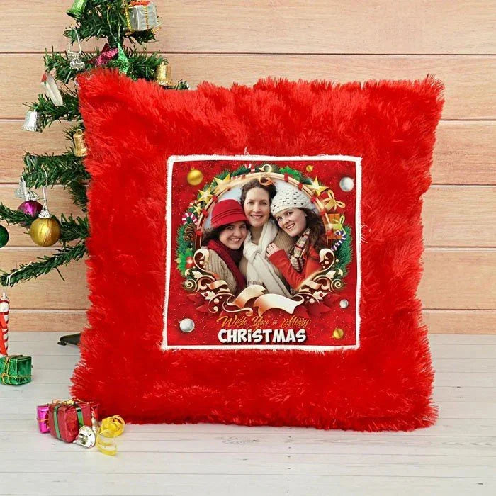 Red Christmas-themed pillow with a photo of two people and 'Merry Christmas' text, placed in front of a decorated Christmas tree.