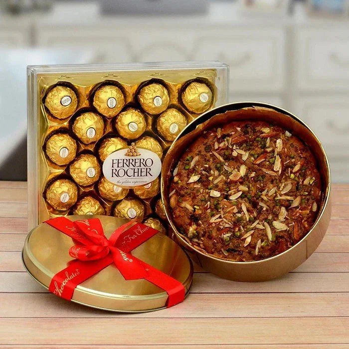Ferrero Rocher chocolate set with a red ribbon next to a fruitcake on a wooden surface.