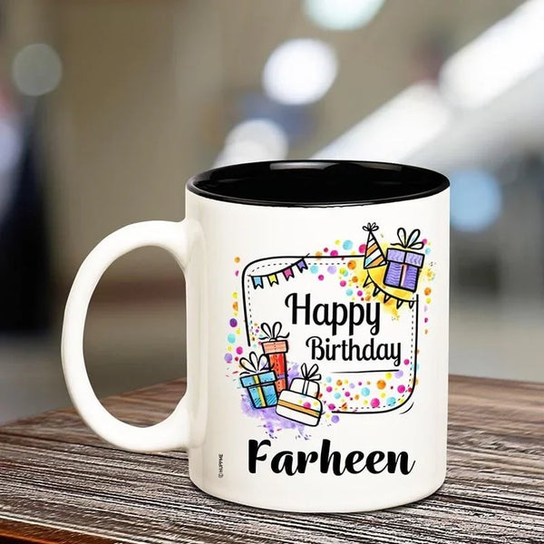 White mug with black interior, featuring colorful birthday design and text 'Happy Birthday Farheen' on a wooden surface.