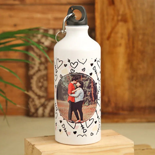 White water bottle with a photo of a couple and heart designs on a wooden surface.