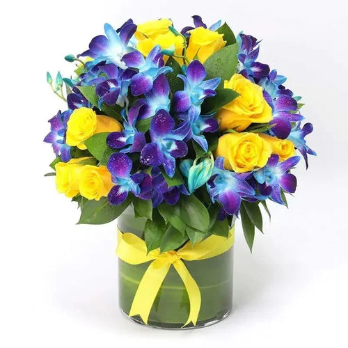 Bouquet of blue and yellow flowers in a clear vase with a yellow ribbon on a white background