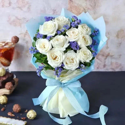 Bouquet of white roses with blue ribbons on a table with snacks.