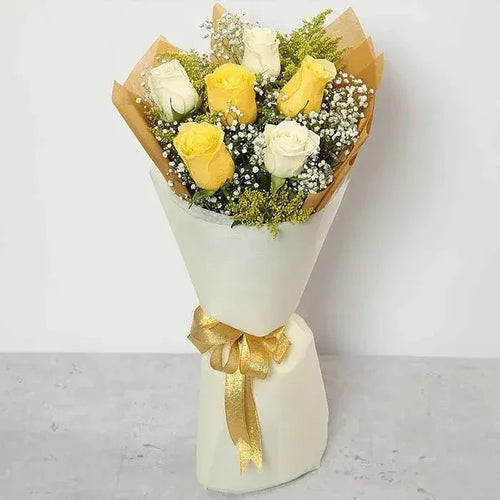 Bouquet of yellow and white roses wrapped in brown paper with a gold ribbon on a light gray background