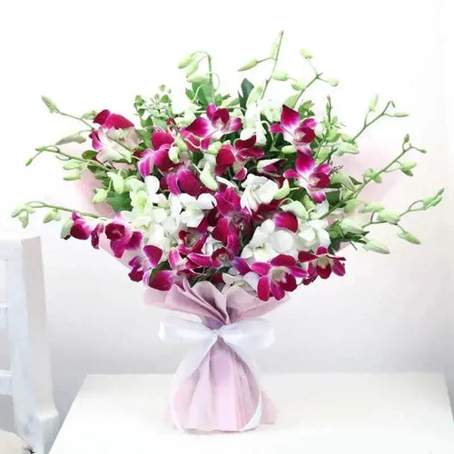 Bouquet of purple and white flowers wrapped in pink paper with a white ribbon on a white background