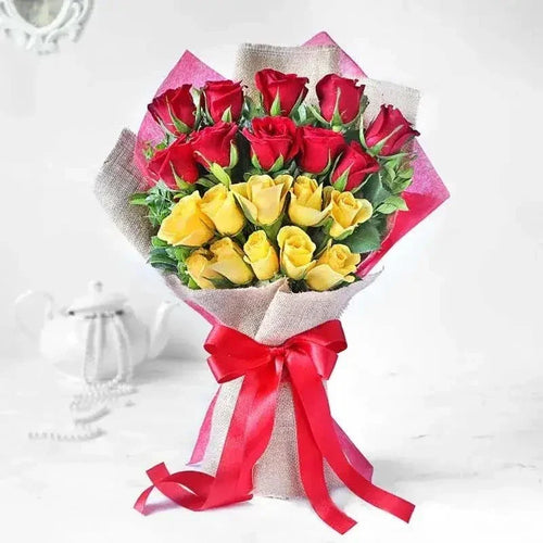 Bouquet of red and yellow roses wrapped in burlap with a red ribbon on a white background