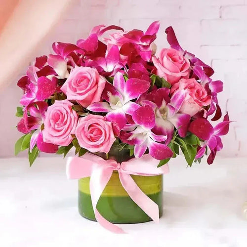 Bouquet of pink roses and purple orchids in a green vase with a pink ribbon on a white background