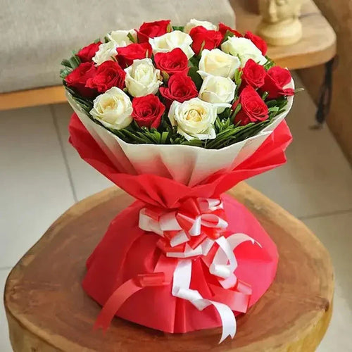 Bouquet of red and white roses wrapped in red paper with a bow on a wooden stool.