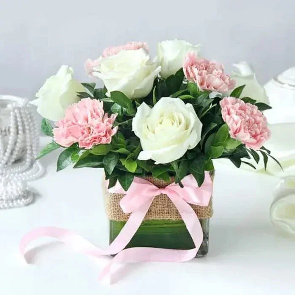 Bouquet of white and pink flowers in a clear vase with a pink ribbon on a light background