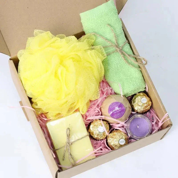 Gift box with yellow loofah, green towel, candles, and chocolates on a white background