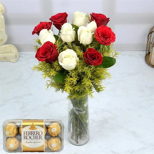Bouquet of red and white roses in a clear vase with a box of Ferrero Rocher chocolates on a light background