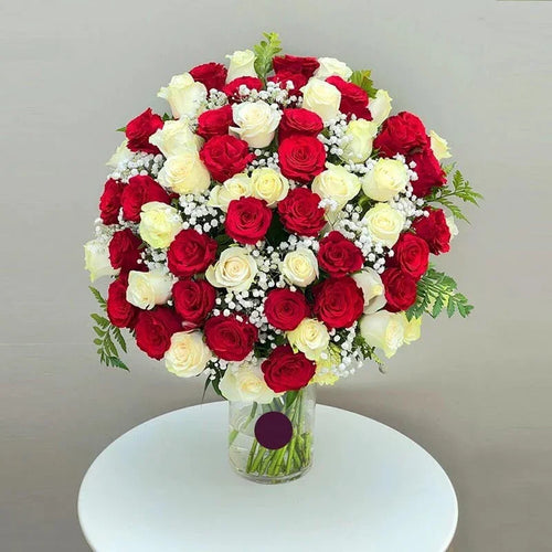 Bouquet of red and white roses in a clear vase on a white surface with a gray background