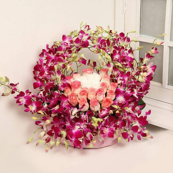 Floral arrangement with pink roses and purple orchids in a decorative container.