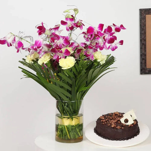 Bouquet of flowers in a vase next to a chocolate cake on a white surface.