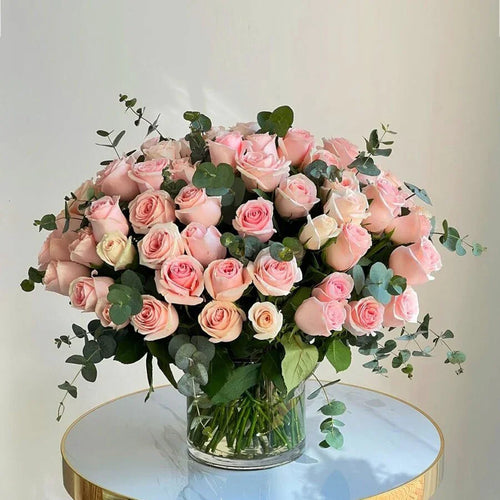 Bouquet of pink roses with greenery in a clear vase on a round table.