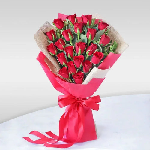 Bouquet of red roses wrapped in pink paper with a red ribbon on a white background
