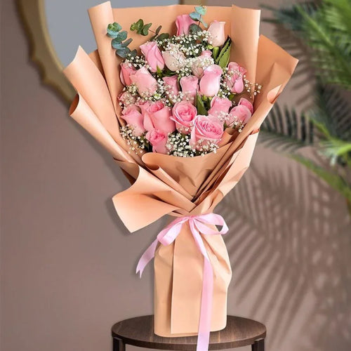 Bouquet of pink roses wrapped in brown paper with a pink ribbon on a wooden stool.