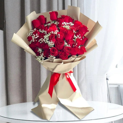 Bouquet of red roses wrapped in beige paper with a red ribbon on a glass table.