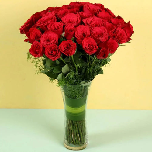 Bouquet of red roses in a clear vase on a light green surface with a yellow background