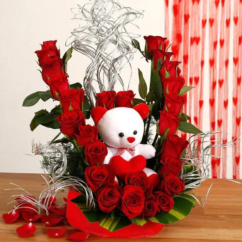Bouquet of red roses with a white teddy bear in the center on a wooden surface.