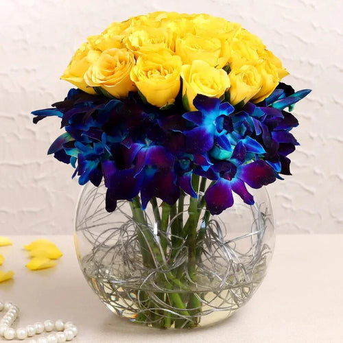 Bouquet of yellow roses and blue orchids in a clear vase on a light background