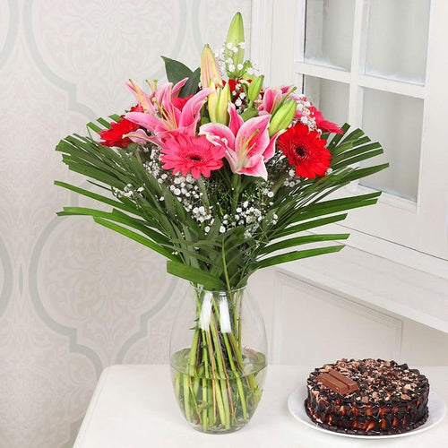 Bouquet of flowers in a vase next to a chocolate cake on a white surface.