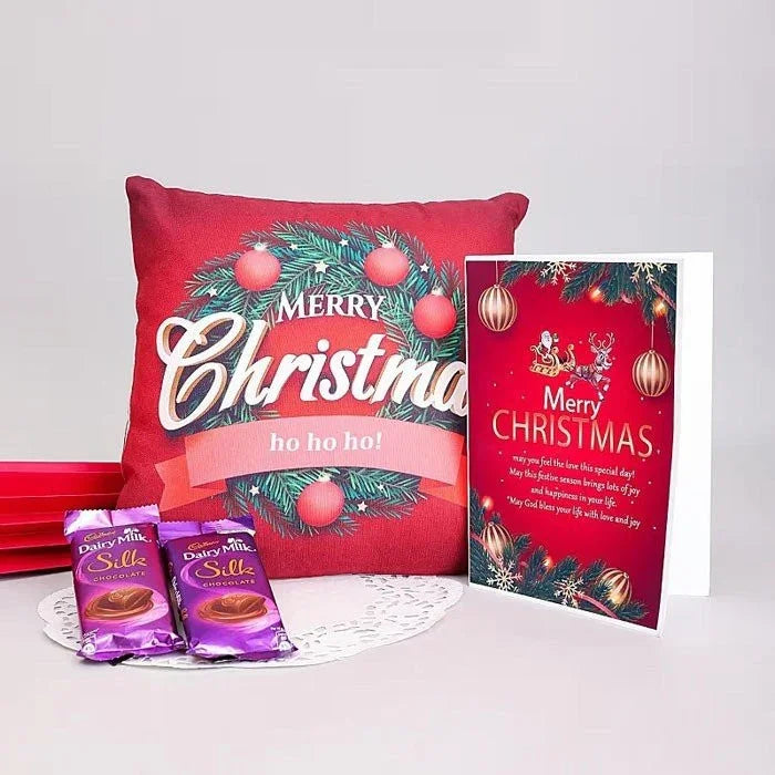 Red Christmas pillow with festive design, two Dairy Milk Silks, and a Christmas card on a white background.
