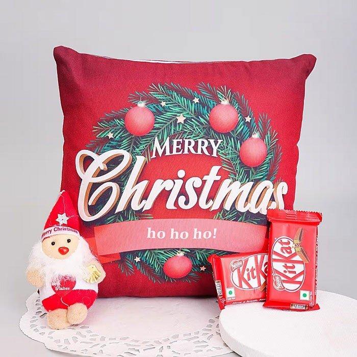 Red Christmas pillow with festive design, small Santa figurine, and KitKat chocolate bars on a light gray background.