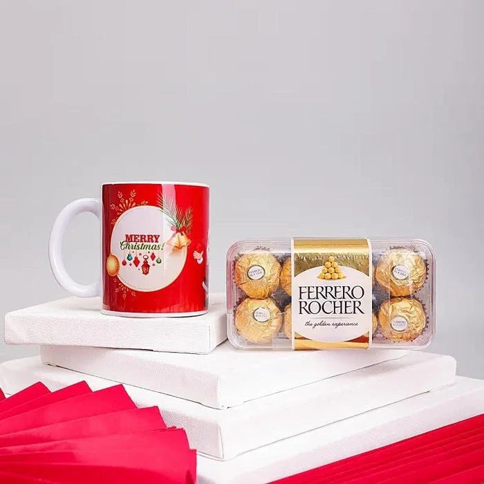 Red mug with 'Merry Christmas!' text and Ferrero Rocher chocolate packaging on a white surface.