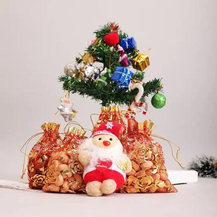 Small Christmas tree with decorations and a plush Santa Claus toy in front of gift bags.