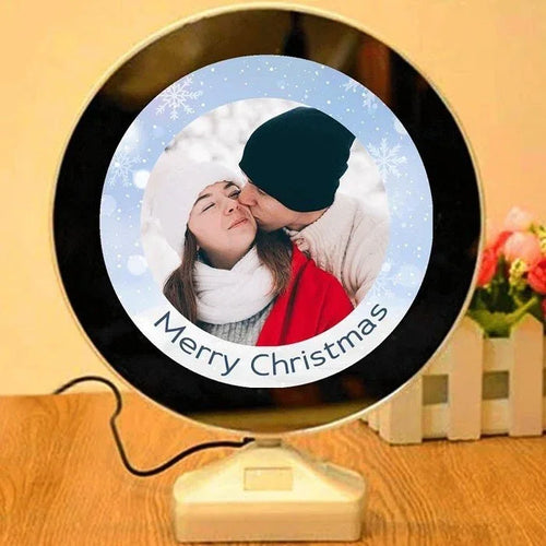 Round decorative item with a photo of two people kissing and 'Merry Christmas' text, on a wooden surface.