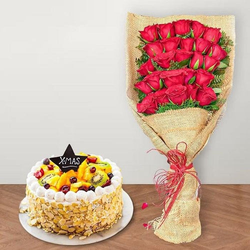 Fruit cake with a 'XMAS' decoration next to a bouquet of red roses on a wooden table.