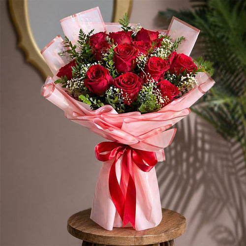 Bouquet of red roses wrapped in pink paper with a red ribbon on a wooden stool.