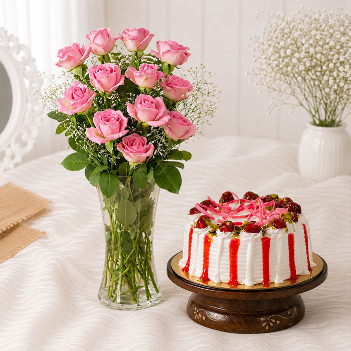 Bouquet of pink roses in a vase next to a decorated cake on a white surface.