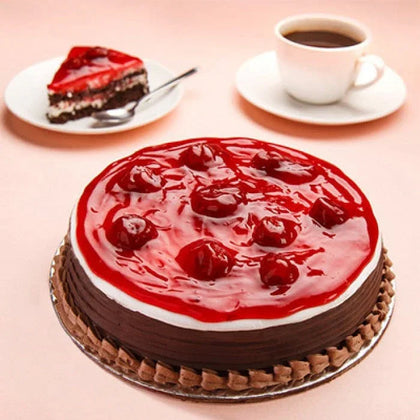 Chocolate cake topped with strawberry glaze and cherries, with a slice and coffee cup beside.