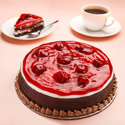Chocolate cake topped with strawberry glaze and cherries, with a slice and coffee cup beside.