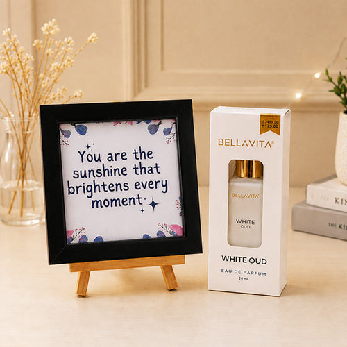 Bellavita White Oud perfume box with a framed quote on a decorative stand.