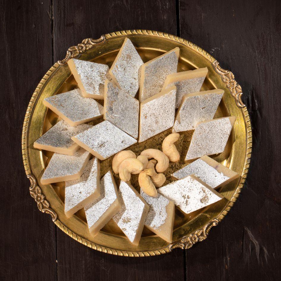 Kaju katli sweets arranged on a golden plate with cashew nuts on a dark wooden background