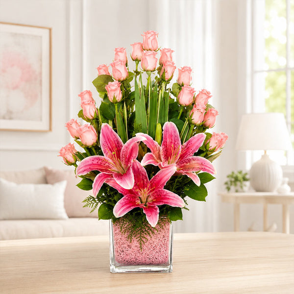 Bouquet of pink lilies and roses in a glass vase on a table with a blurred indoor background