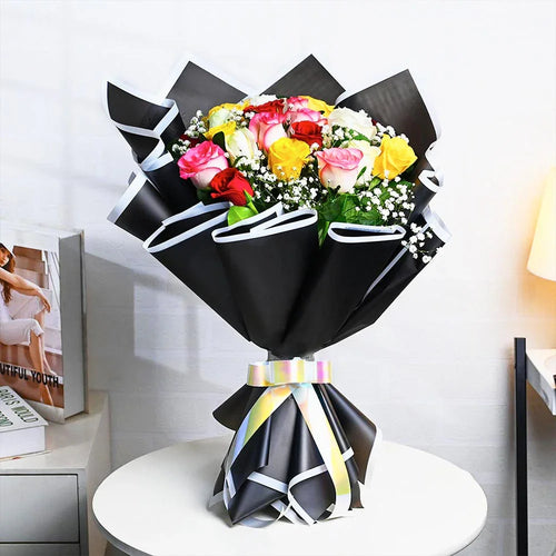 Bouquet of flowers wrapped in black paper with a colorful ribbon on a white surface.